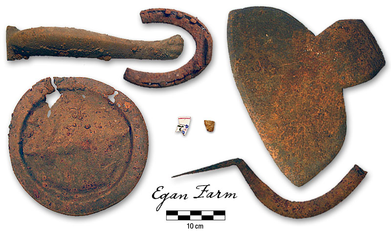 Photograph of effigy pipe bowl, ceramic teacup, shanty plate, stove leg, broken horseshoe with nails, reaping hook, broad axe
